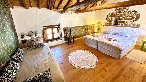 Um quarto aconchegante com teto de madeira, parede de pedra, uma cama, um sofá e uma pequena mesa.