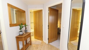 A hallway with wooden flooring, a wooden console table with a potted plant, and a mirror on the wall. - Seabreeze Suites (Southampton)