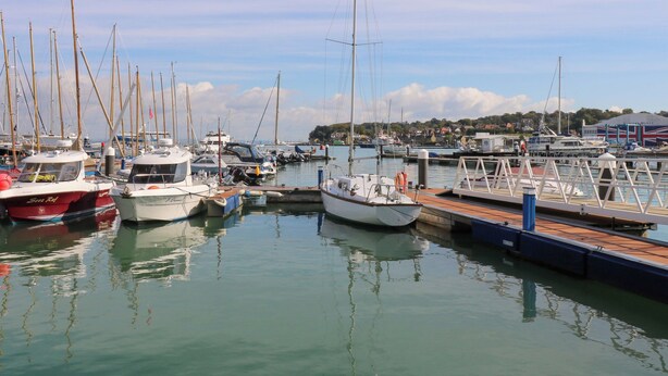 A marina with various boats docked, a pier, and a building with a flag. - Seabreeze Suites (Southampton)