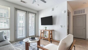 Una sala moderna con un sofá, una mesa de centro de madera, una silla y un televisor montado en la pared.