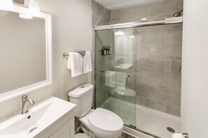 A modern bathroom with a glass-enclosed shower, a white sink, and a toilet.
