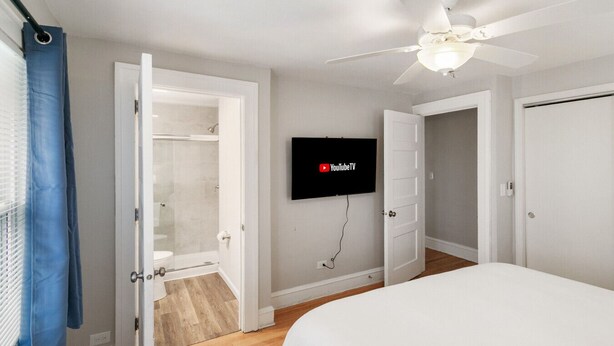 A bedroom with a bed, a ceiling fan, a TV mounted on the wall, and a closet with a shower. - Highwood Haven- 4 Bedroom Steps to Train station! (Highwood)