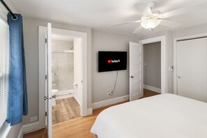 Un dormitorio con cama, ventilador de techo, televisor montado en la pared y armario con ducha.