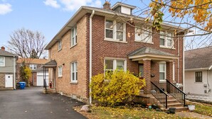 A two-story brick house with a front porch, a garage, and a small yard with autumn leaves. - Highwood Haven- 4 Bedroom Steps to Train station! (Highwood)