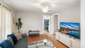 A modern living room with a sofa, coffee table, TV, and a view of the cityscape. - Highwood Haven- 4 Bedroom Steps to Train station! (Highwood)