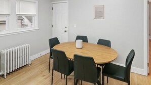 A room with a round wooden table surrounded by six chairs, a white radiator, and a door with a window above it. - Highwood Haven- 4 Bedroom Steps to Train station! (Highwood)