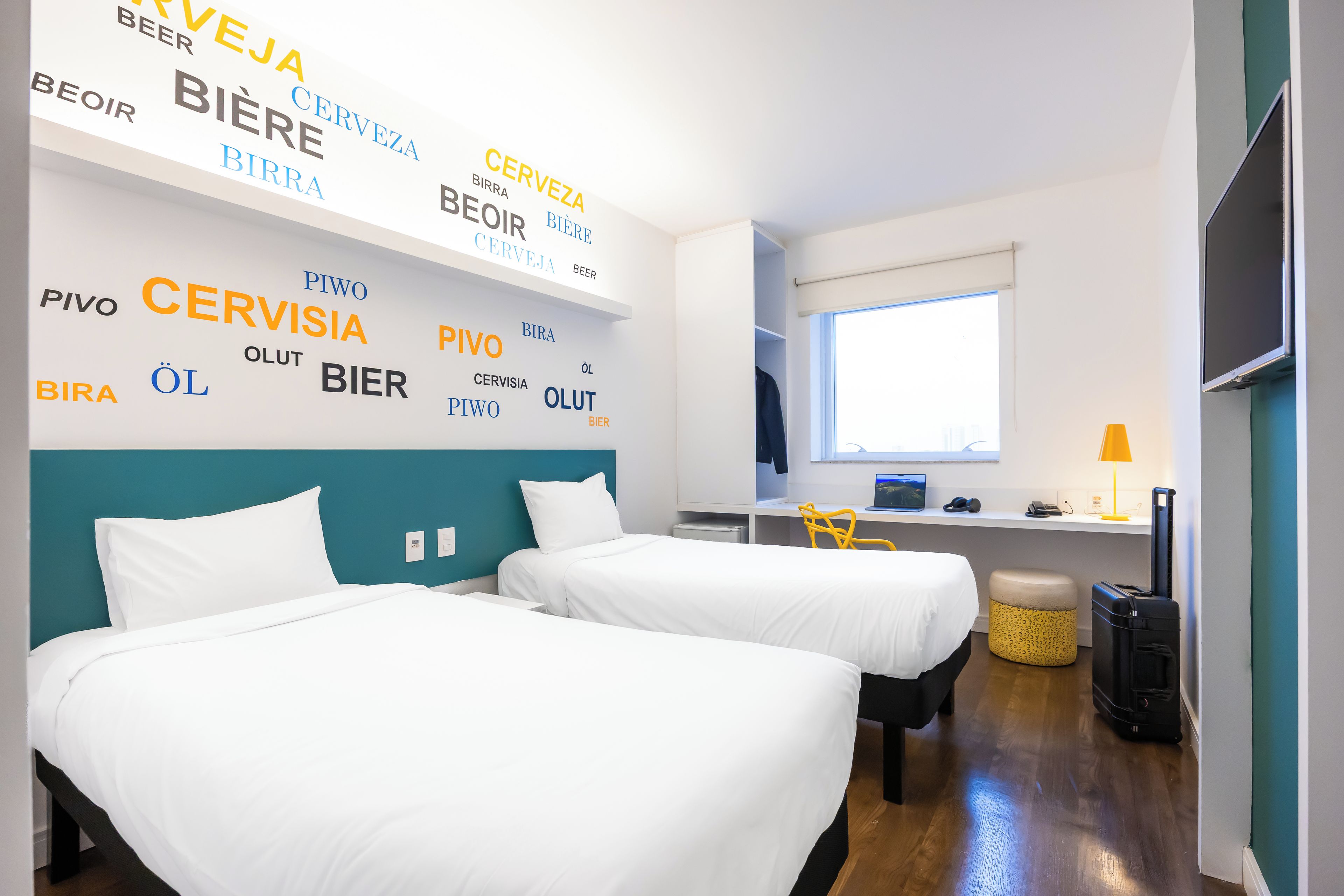 A hotel room with two beds, a desk with a computer, and a window.