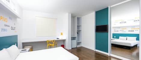Quarto de hotel moderno com cama, escrivaninha, cadeira e televisão.
