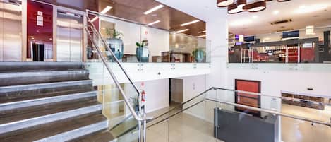 Un interior moderno con una escalera de cristal, techo de madera y un área de comedor visible a través del vidrio.