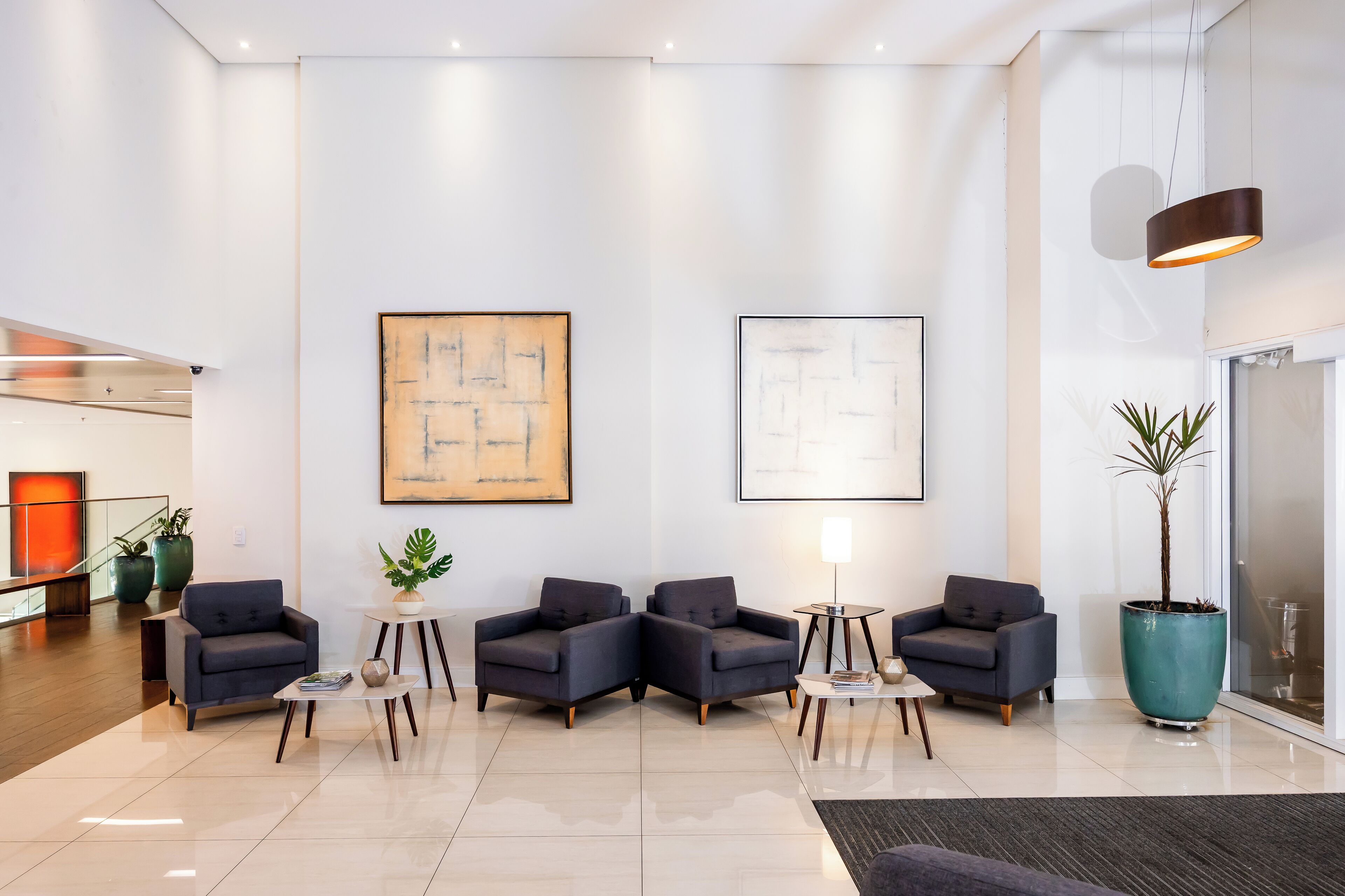 Um lobby moderno com área de estar, duas grandes pinturas abstratas e um vaso de planta.