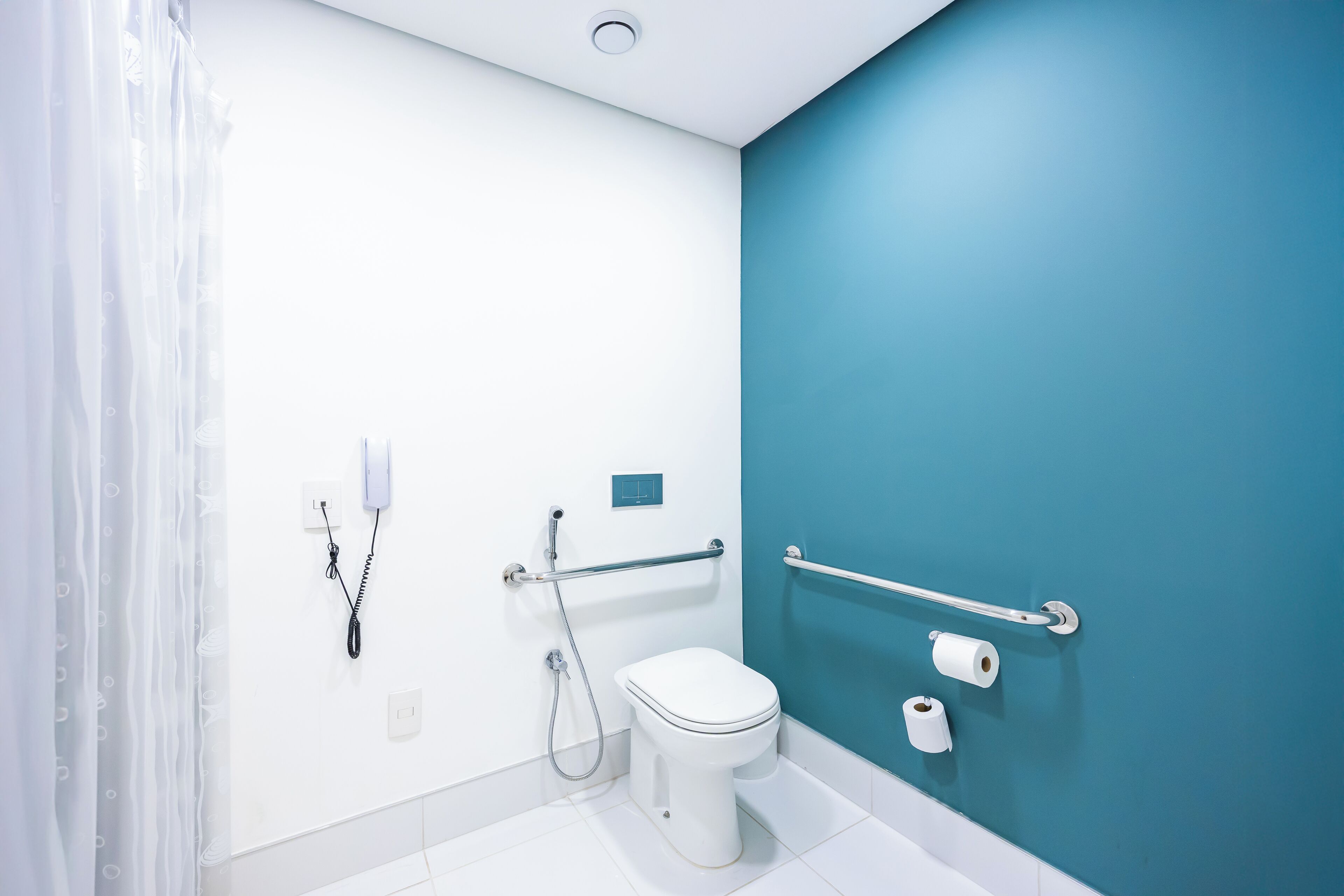 Une salle de bain moderne avec des toilettes blanches, un mur d’accent bleu et une barre d’appui.
