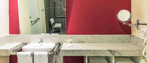 A bathroom with a granite countertop, two sinks, a mirror, a towel rack, and a shower area.