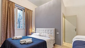 A bedroom with a large bed, a smaller bed, a window with curtains, and a door. - Orchid Room – Double with Wi-Fi, A/C, and Accessible Bathroom (Prato)