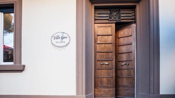 A double wooden door with a metal handle, a small window with a brown frame, and a sign on the wall reading 'Villa Gove ROOMS'. - Orchid Room – Double with Wi-Fi, A/C, and Accessible Bathroom (Prato)