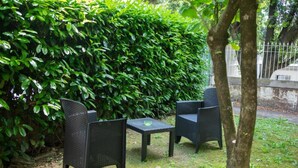 Een terras met twee stoelen en een tafel, omgeven door weelderige groene begroeiing.