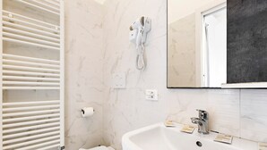 Een badkamer met een witte wasbak, een spiegel, een handdoekhouder en een föhn aan de muur.