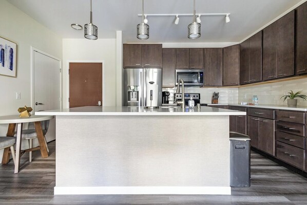 A modern kitchen with a large island, stainless steel appliances, and dark wooden cabinets. - Landing | Chic 1BD, Clubhouse, Gym (Milwaukee)