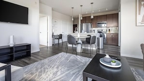 A modern living room with a flat-screen TV, a dark wood dining table, and a gray patterned rug. - Landing | Amazing 2BD, Gym, Clubhouse (Milwaukee)