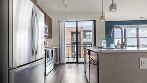 A modern kitchen with stainless steel appliances, a large island, and a view of the city through the sliding glass door. - Landing | Amazing 2BD, Gym, Clubhouse (Milwaukee)