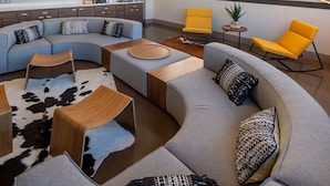 A modern living room with a curved sofa, a small coffee table, and two yellow chairs. There are abstract wall art pieces and a large window with blinds. - Landing | Amazing 2BD, Gym, Clubhouse (Milwaukee)
