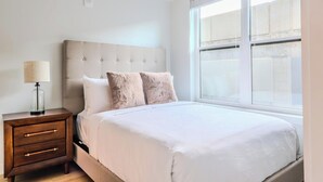 Une chambre à coucher avec un lit, une table de chevet, une lampe et une fenêtre.