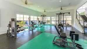 A spacious gym with various exercise machines, large windows, and a staircase.