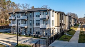 Ein mehrstöckiges Apartmenthaus mit Balkonen, einem Parkplatz und einem gepflegten Rasen.