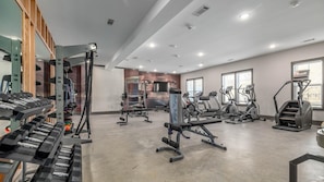 Ein Fitnessraum mit verschiedenen Trainingsgeräten, darunter Laufbänder, Crosstrainer und Kurzhanteln.