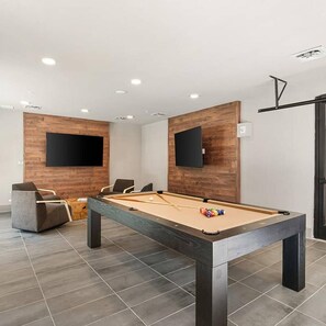 A pool table in a room with wooden panel walls and a flat-screen TV mounted on each wall. - Landing | Beautiful 1BD, Gym, Pool (Savannah)