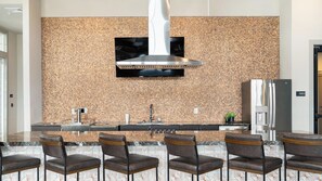 Une cuisine moderne avec un revêtement mural en pierre, des appareils en acier inoxydable et un coin bar doté de chaises en cuir.