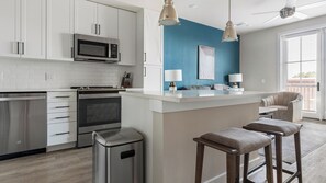 A modern kitchen with white cabinetry, a built-in microwave, a stainless steel oven, and a small island with bar stools. - Landing | Beautiful 1BD, Gym, Pool (Savannah)
