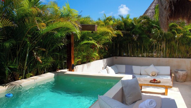 A poolside area with a lounge chair and a small table, surrounded by lush tropical plants. - Ph 10mins from tulum beach, with private pool and spa, ideal for families. (Tulum)