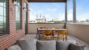 Uma varanda com mesa e cadeiras, um sofá e vista para o horizonte da cidade.