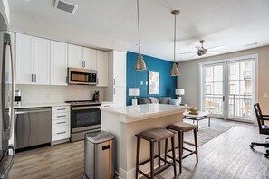 A modern kitchen with white cabinets, a central island, stainless steel appliances, and a blue accent wall. - Landing | Spectacular Studio, Pool, Game Room (Savannah)