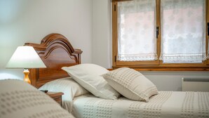 Un dormitorio con cabecera de madera, una mesita de noche con lámpara y una ventana con cortinas de encaje.