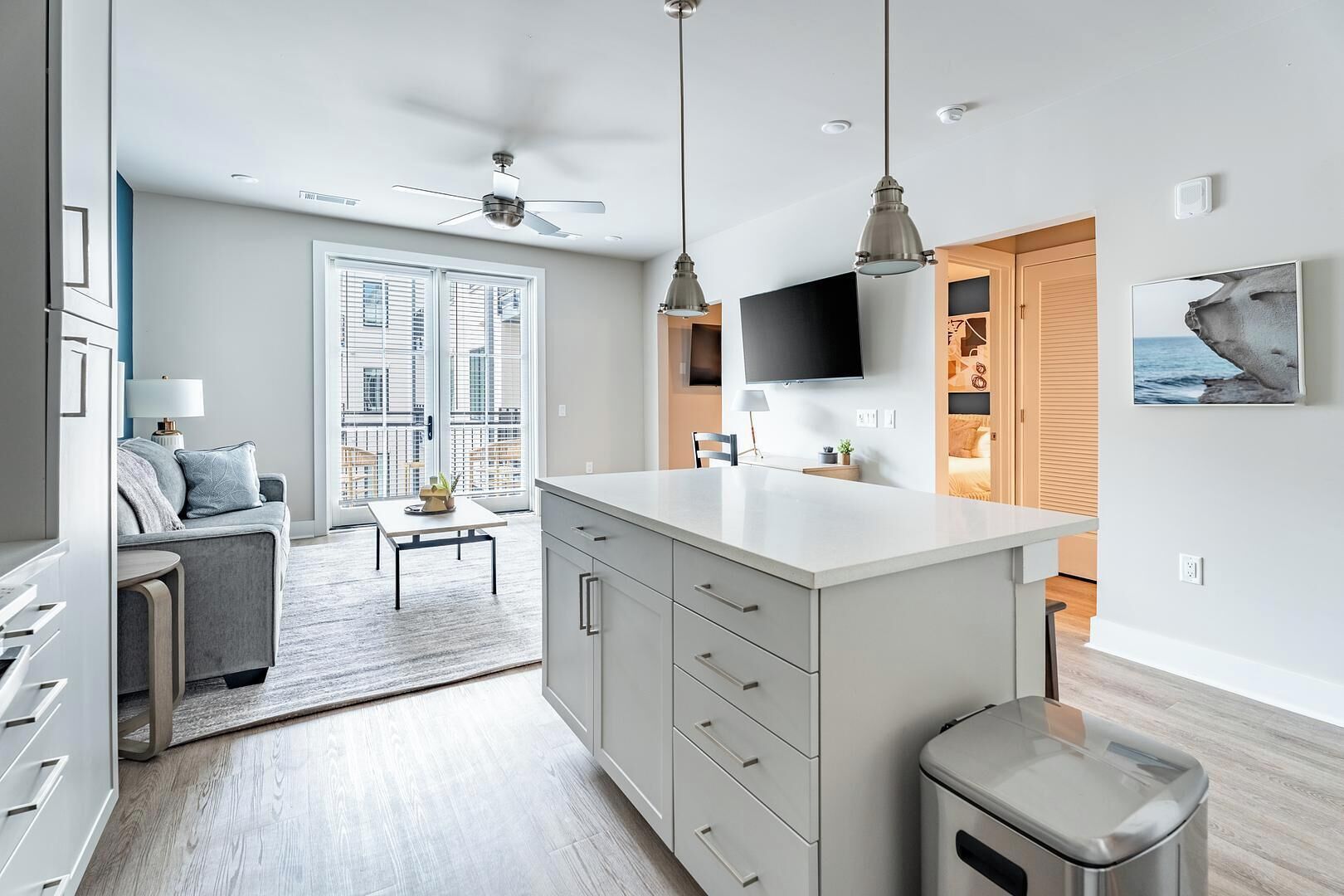 A modern kitchen with a central island, a dining area with a table and chairs, a sofa, and a TV mounted on the wall.