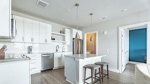 A modern kitchen with white cabinetry, a central island, and bar stools. - Landing | Chic 2BD, Pool, Yoga Studio (Savannah)