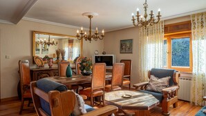 A traditional room with a wooden dining table, chairs, a sofa, a television, and a chandelier. - Apartment 'Casa Geli 2' in La Robellada, Onís – Up to 9 Guests, 4 Bedrooms, 2 Bathrooms (La Robellada)