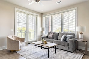 A living room with a grey sofa, a beige armchair, a coffee table, and two side tables with lamps. - Landing | Spectacular 2BD, Yoga Studio, Pool (Savannah)