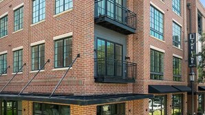 A multi-story brick building with large windows and a covered entrance area. - Landing | Spectacular 2BD, Game Room, Pool (Savannah)