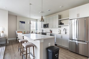 A modern kitchen with a central island, stainless steel appliances, and pendant lighting. - Landing | Spectacular 2BD, Yoga Studio, Pool (Savannah)