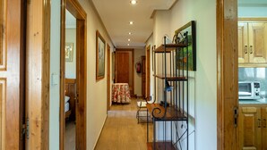 Un couloir avec des portes en bois, une table à manger recouverte d’une nappe à motifs floraux et un coin cuisine avec des placards en bois et un four à micro-ondes.