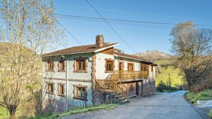 Un bâtiment en pierre de deux étages, doté d’un balcon, d’un escalier et d’une allée pavée menant à une route de campagne.