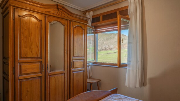 Une chambre avec une armoire en bois, un lit simple, une fenêtre donnant sur un espace verdoyant et une chaise.