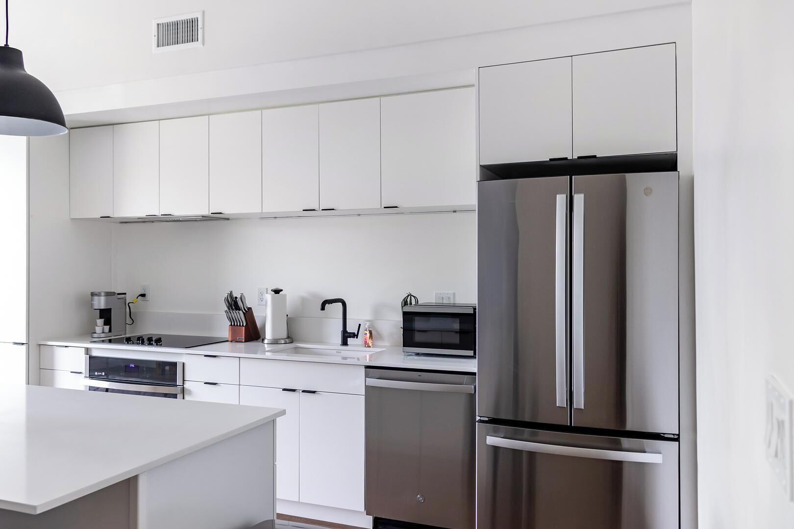 A modern kitchen with white cabinetry, a stainless steel refrigerator, a microwave, and a coffee maker.