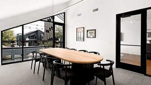 A modern conference room with a large table, black chairs, and large windows offering a view of buildings and greenery. - Landing | Incredible 1BD, Gym, Rooftop Lounge (South Salt Lake)