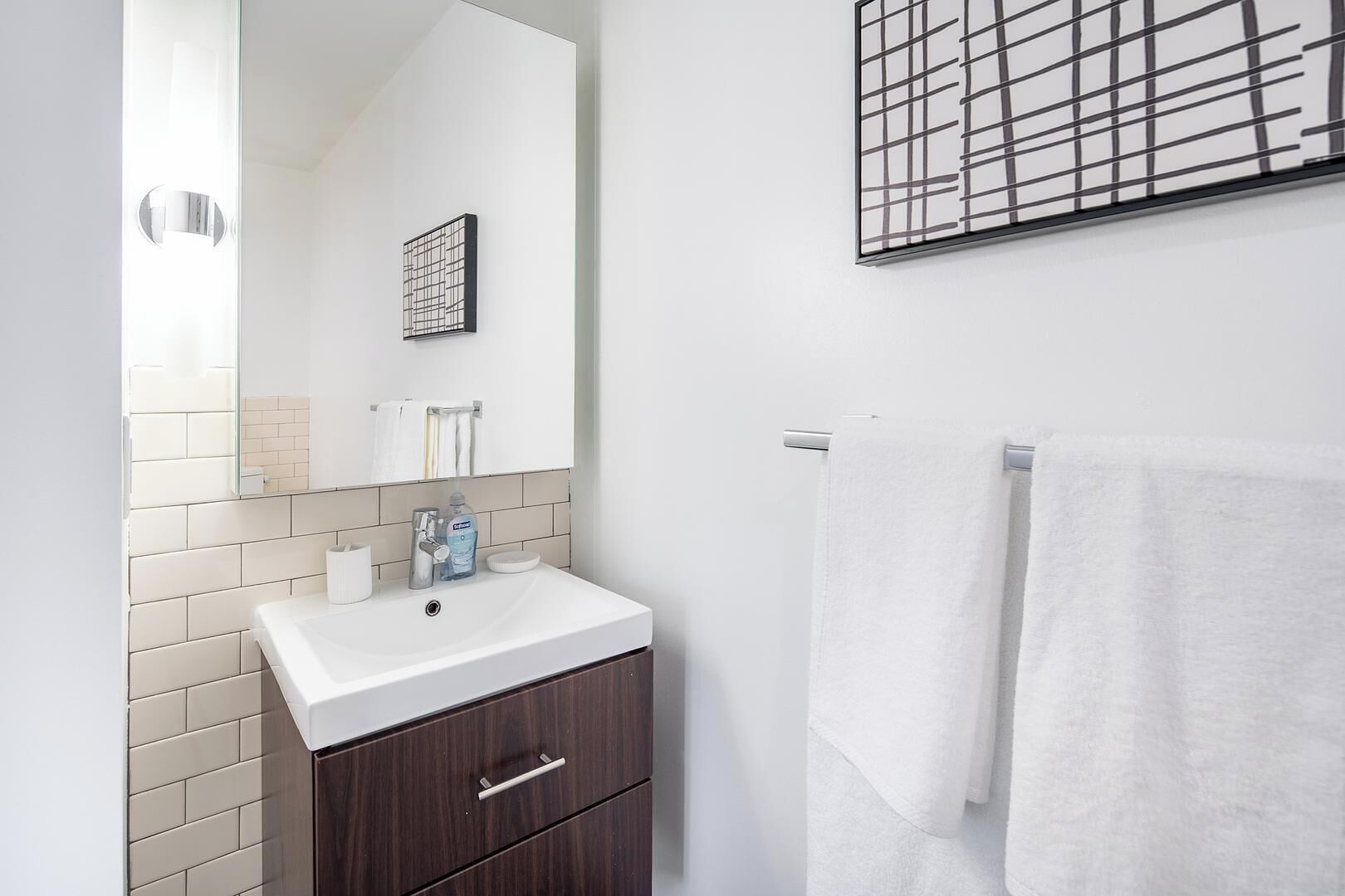 Een moderne badkamer met een witte wasbak, een donker houten kastje, en een handdoek aan een rek.