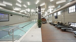 Une piscine intérieure dotée d’une terrasse en bois, de chaises longues et d’un escalier menant aux niveaux supérieurs.