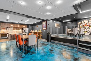 Une cuisine moderne avec des meubles de couleur sombre, un coin repas avec des chaises orange et un sol carrelé de bleu.