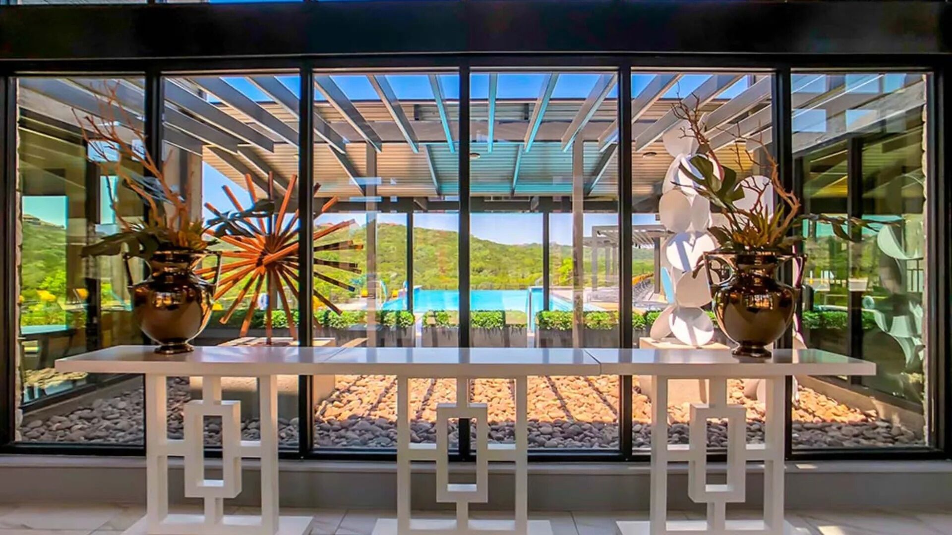 Interior moderno com parede de vidro que oferece vista para uma piscina e paisagem externa.